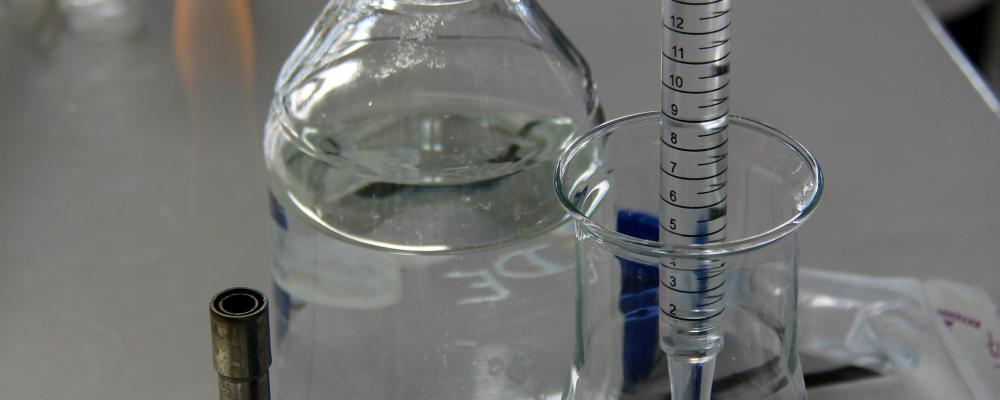 En tekniker häller vätska i en Erlenmeyerkolv med en graderad pipett i ett laboratorieutrymme. Foto: Nathan Rimoux/Unsplash