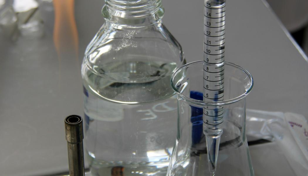 En tekniker häller vätska i en Erlenmeyerkolv med en graderad pipett i ett laboratorieutrymme. Foto: Nathan Rimoux/Unsplash